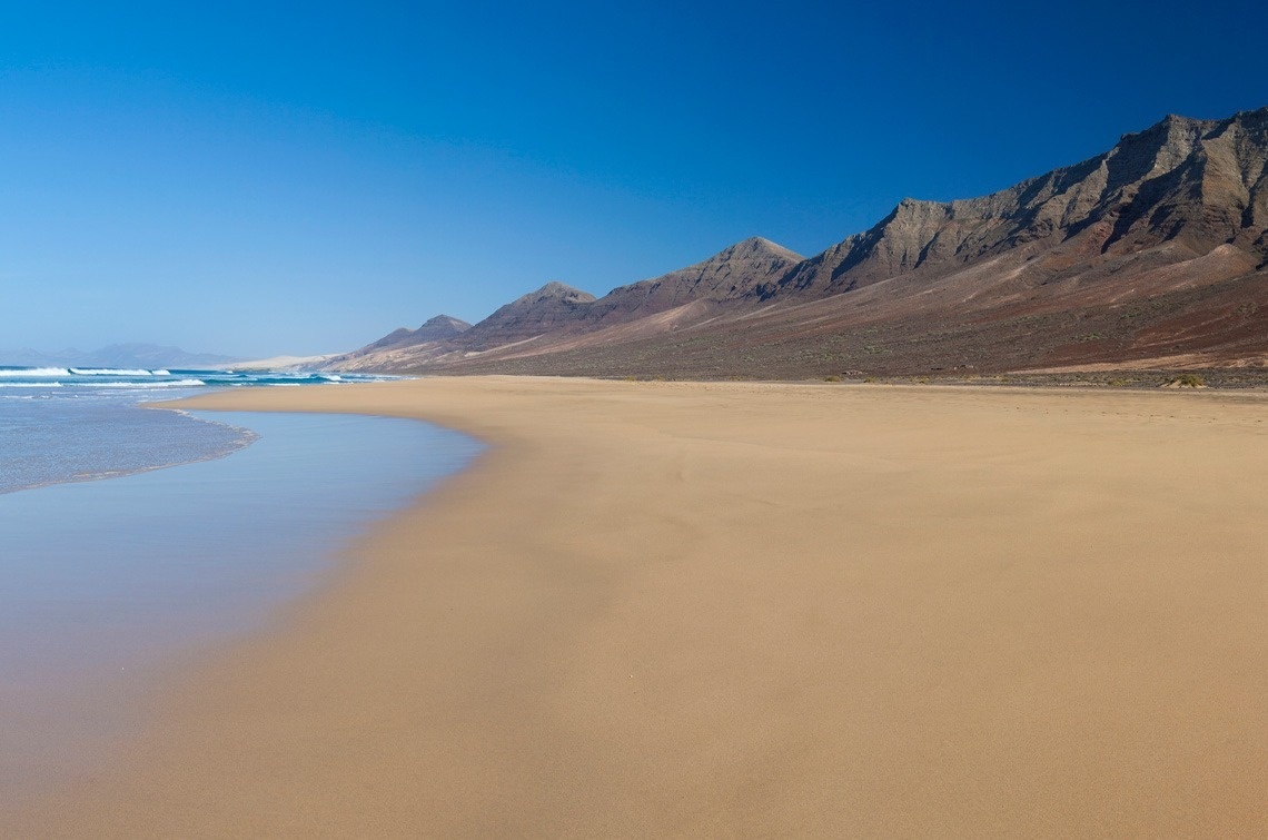 a beach with mountains in the background and a blue sky