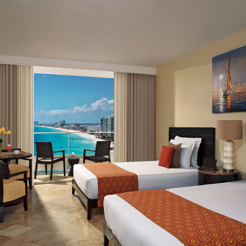 Hotel room with two beds, ocean view balcony, and seating area. DEMO 3