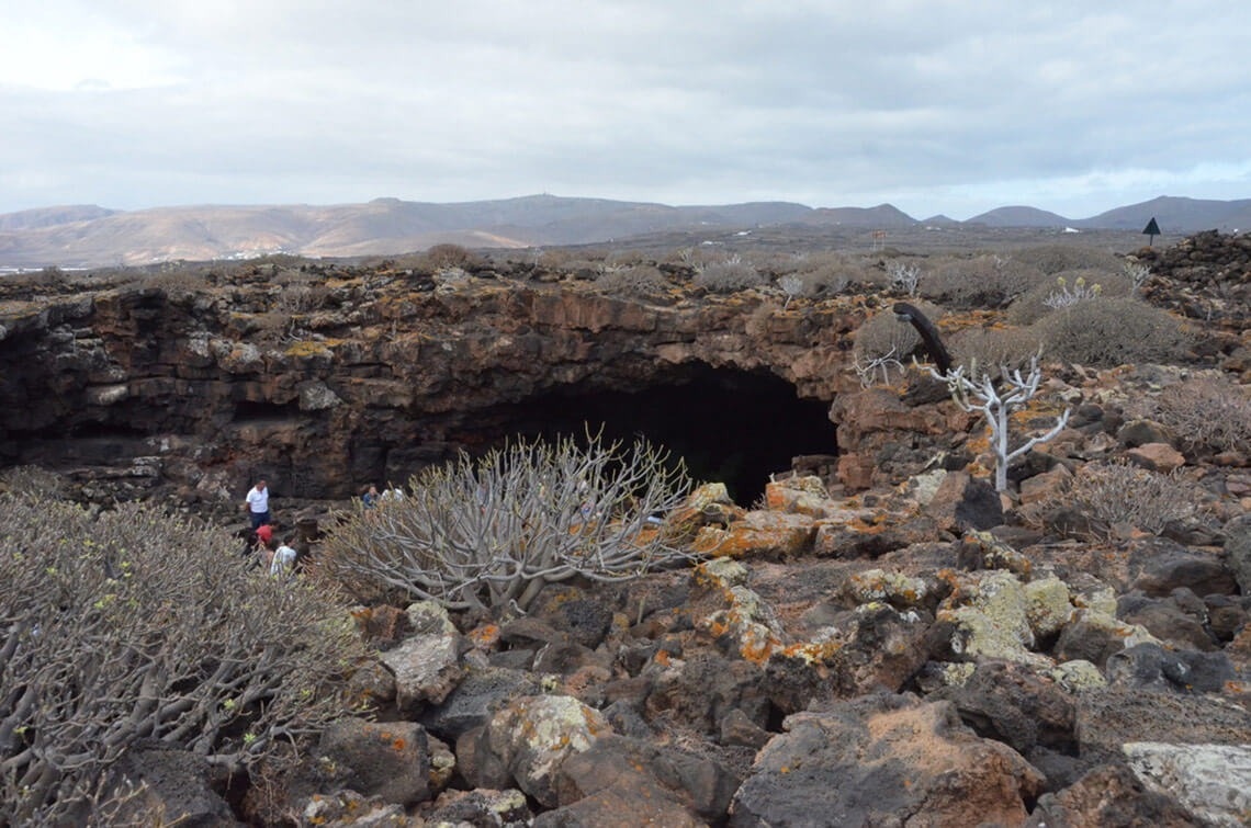 a group of people standing in front of a cave with mountains in the background