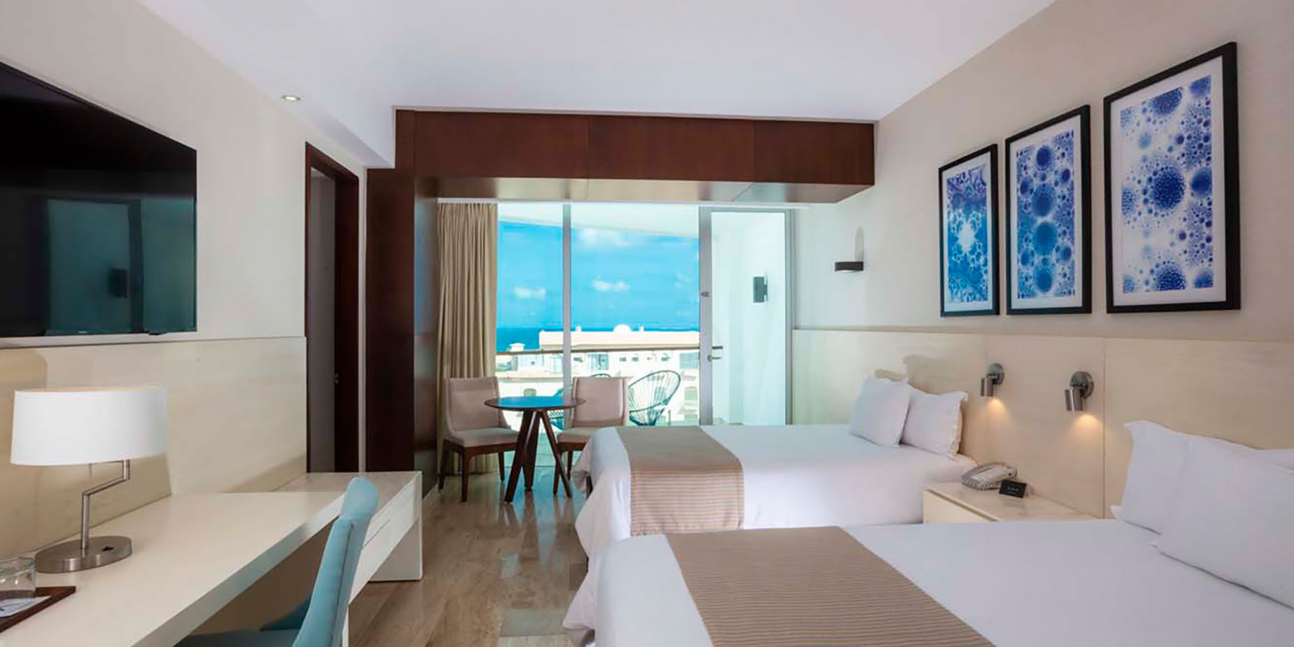 Modern hotel room with two beds, ocean view balcony, desk, and TV. DEMO 3