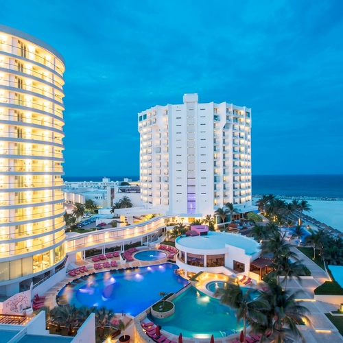 Luxury resort with curved hotel DEMO 3, pools, and beach at dusk