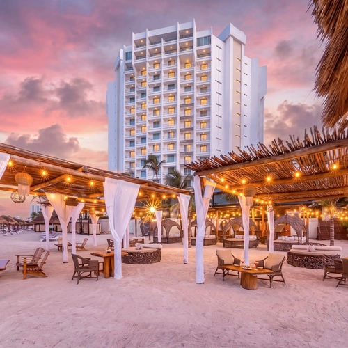 Tropical resort beach cabanas with resort hotel DEMO 3 in background at sunset.