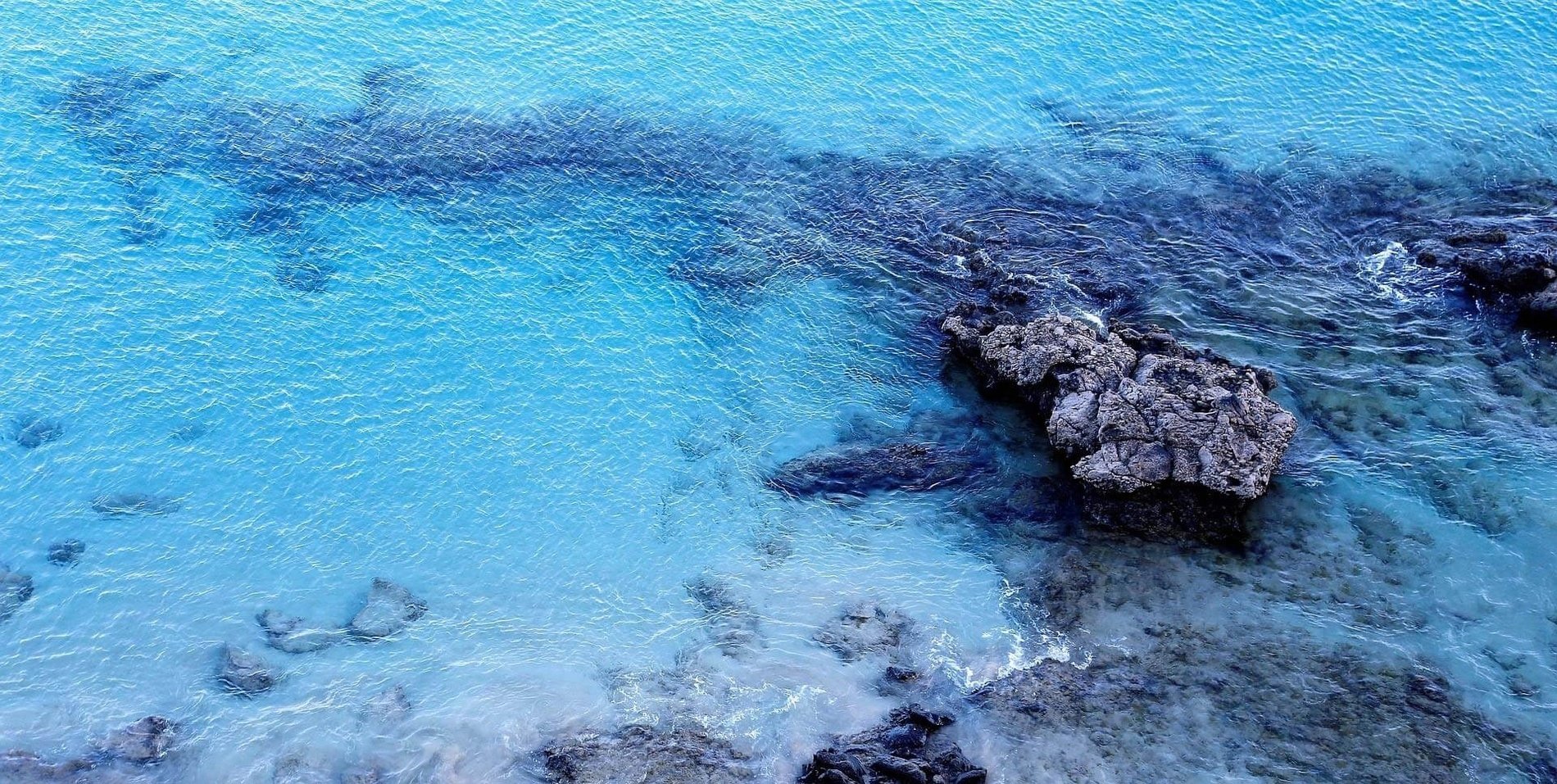 una vista aérea de un océano azul con rocas en la orilla