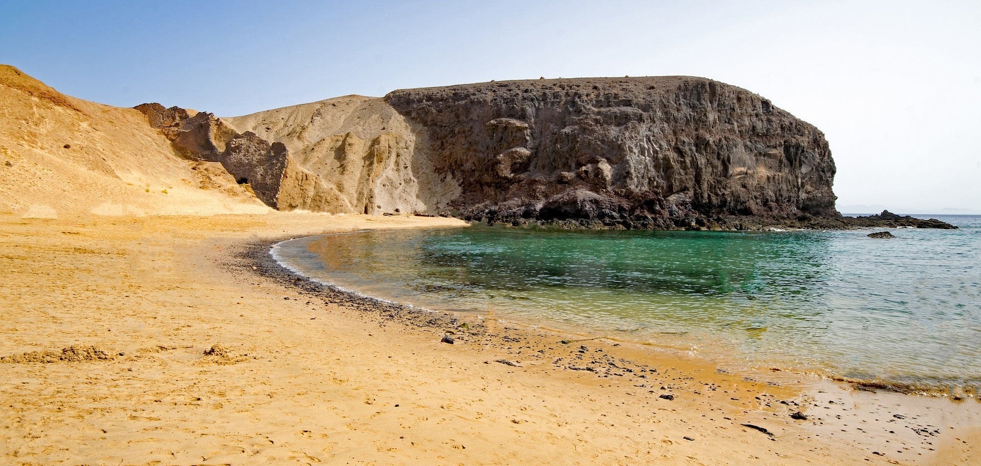 a beach with a large rock in the background