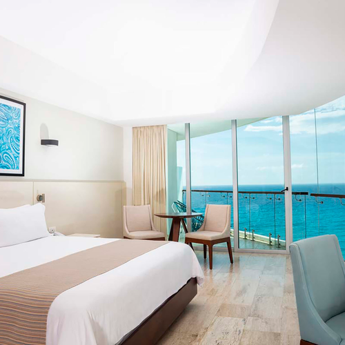 Hotel room with king bed, ocean view balcony, desk, and seating. DEMO 3