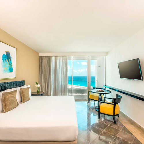 Modern hotel room with ocean view, king bed, and seating area. DEMO 3