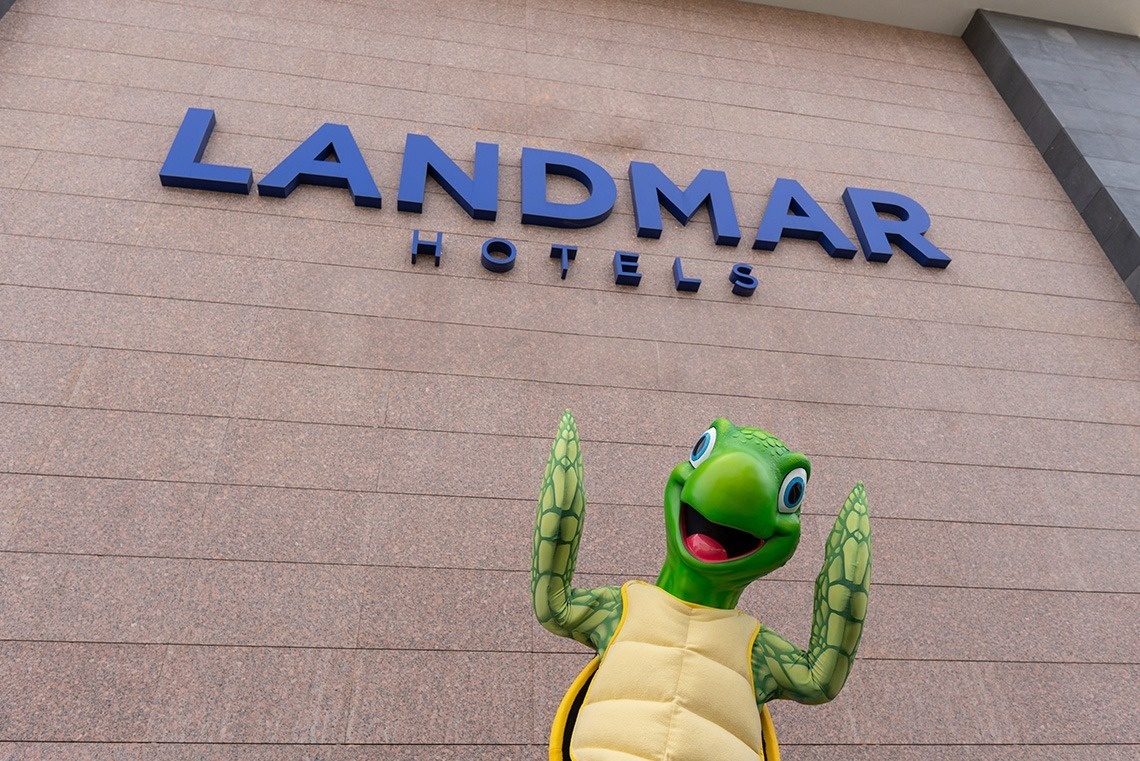 une mascotte de tortue se tient devant le logo de l' hôtel landmar