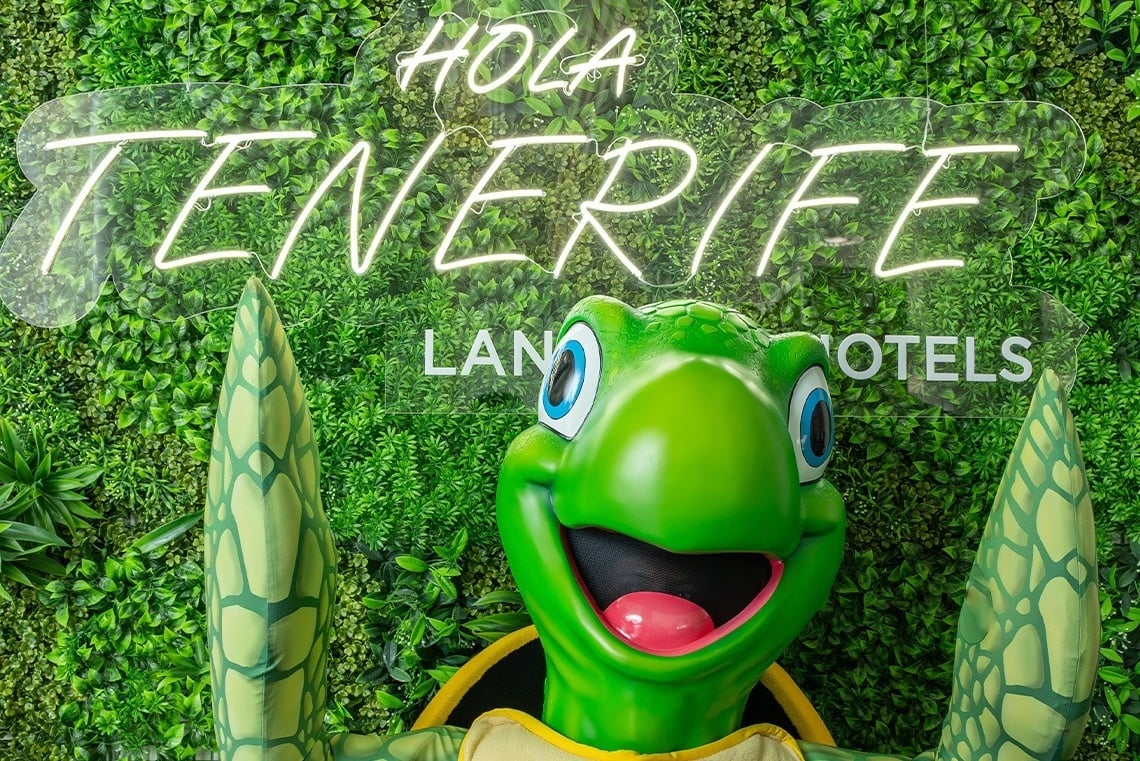 una tortuga de dibujos animados está parada frente a un letrero que dice hola tenerife