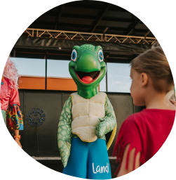 una niña se para frente a una mascota de tortuga que lleva pantalones de playa