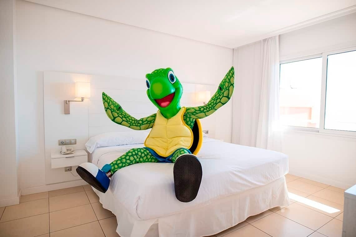 une mascotte de tortue est assise sur un lit blanc