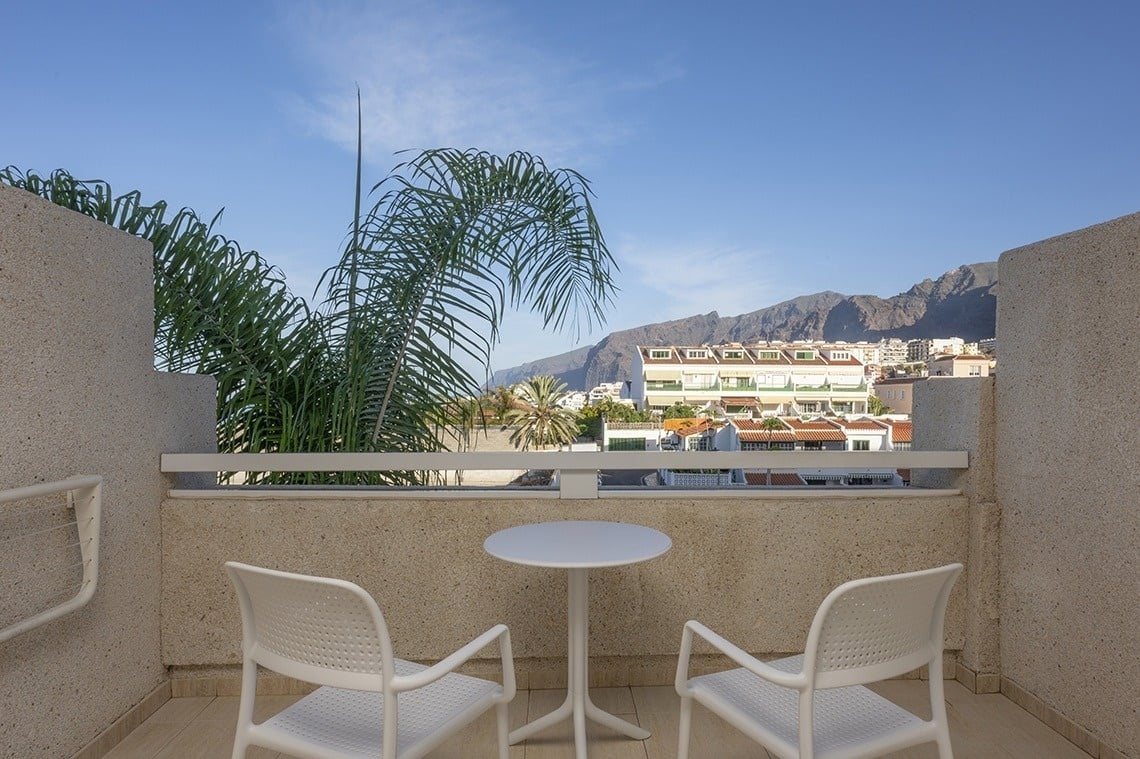 a balcony with two chairs and a table with mountains in the background