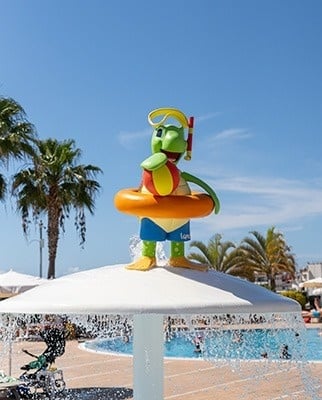 eine Skulptur eines Frosches , das einen Ball hält , steht auf einem Regenschirm in einem Pool .