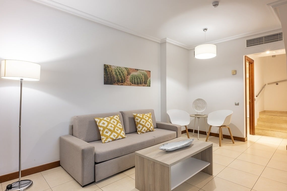 un salon avec un canapé et des chaises et un tableau de cactus au mur