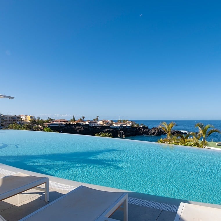 Zwei Gläser mit Cocktails stehen neben einem Pool