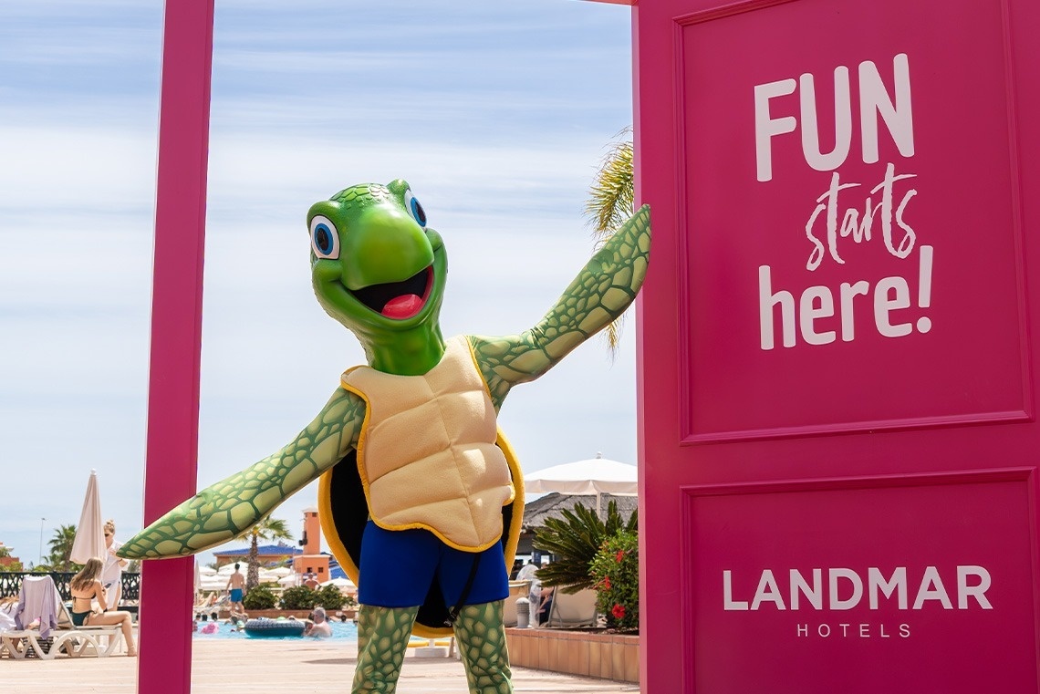 una mascota de tortuga se para frente a una puerta rosa que dice 