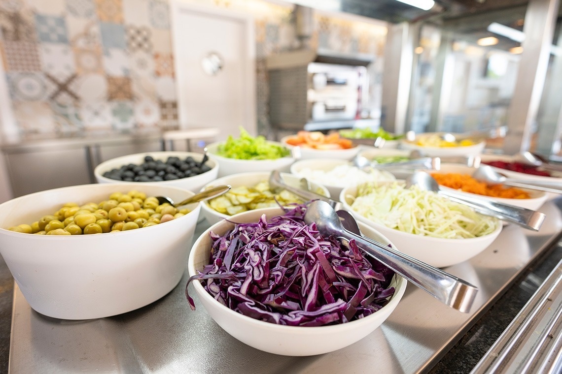 a buffet line with bowls of vegetables including purple cabbage and olives