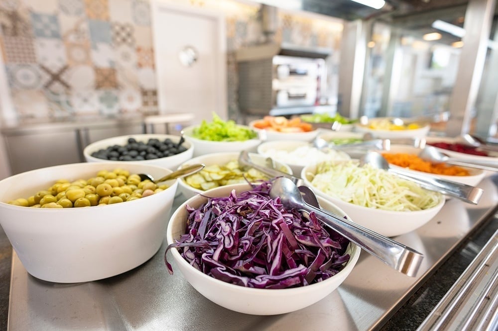 a buffet line with bowls of vegetables including purple cabbage and olives