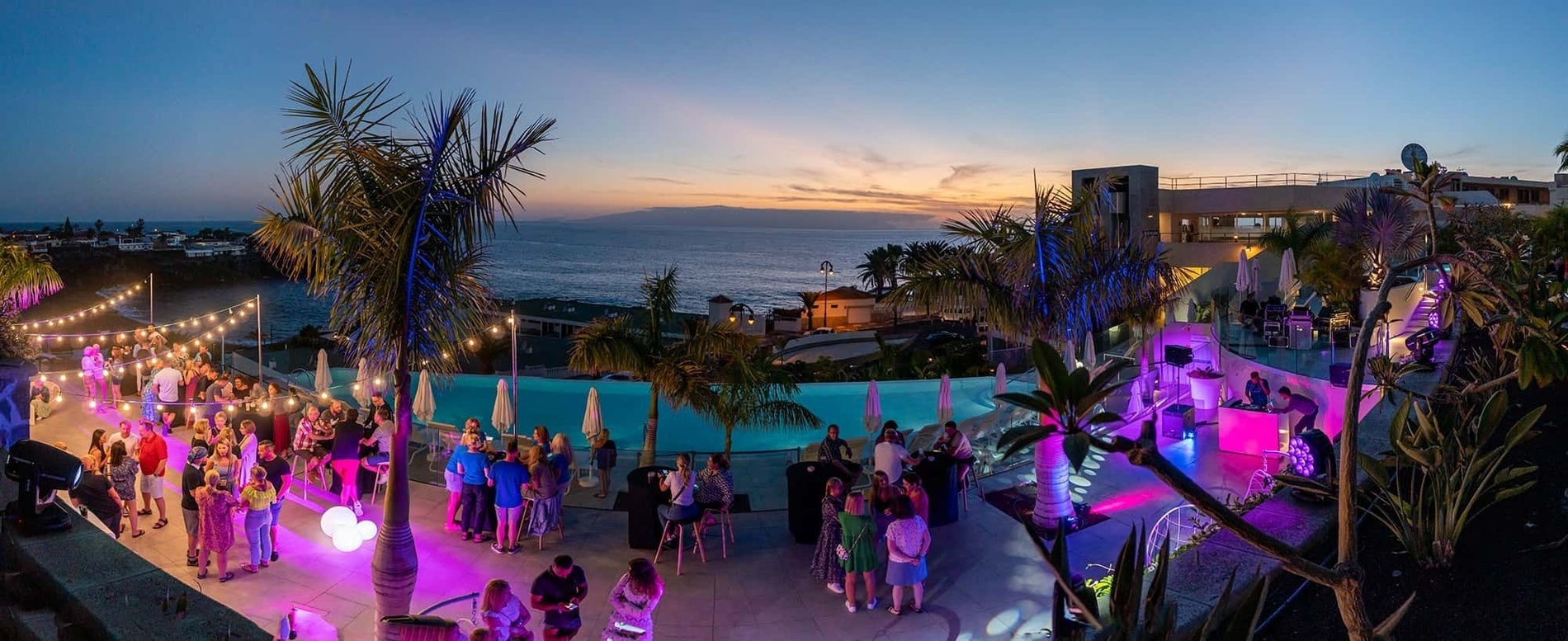 una gran multitud de personas se reúnen alrededor de una piscina al atardecer