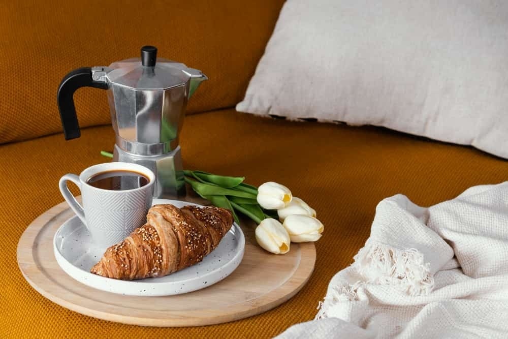 a tray with a croissant , coffee and tulips on a couch .