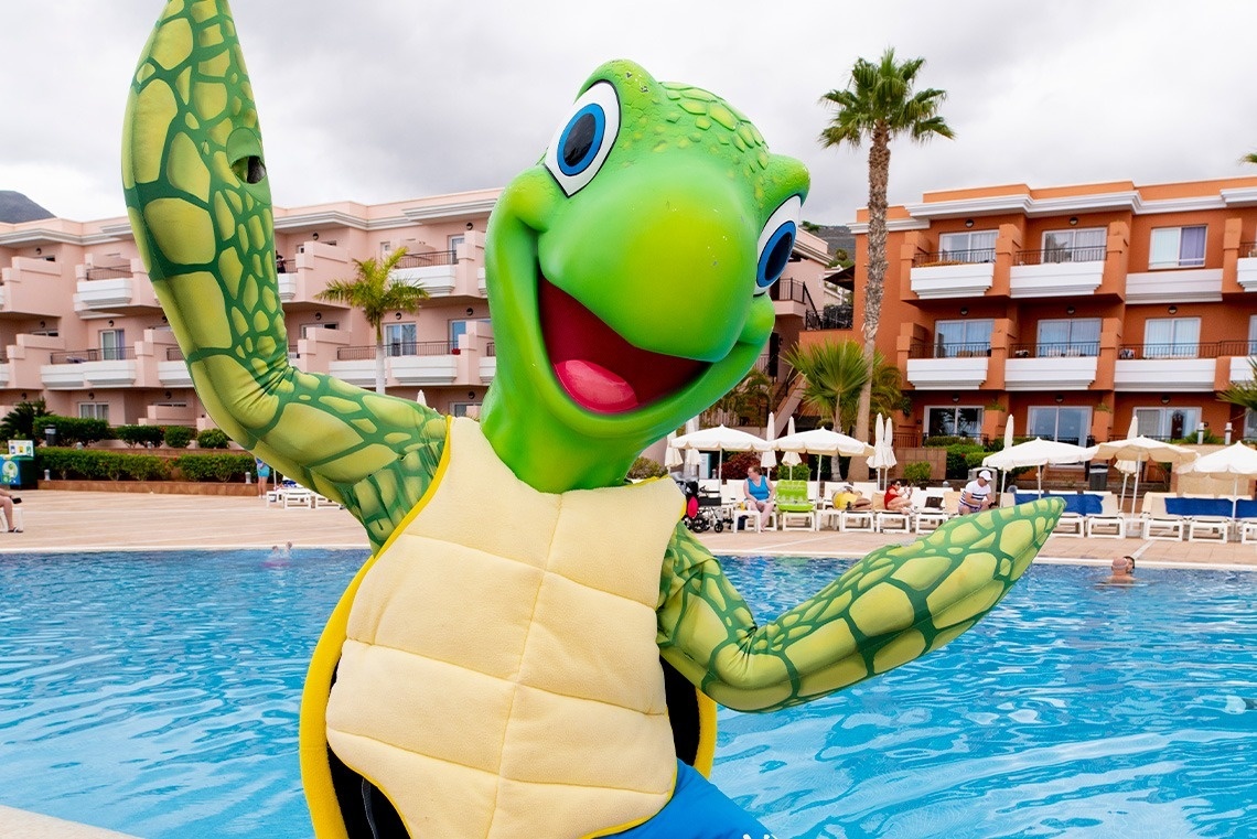 une mascotte de tortue verte se tient à côté d' une piscine