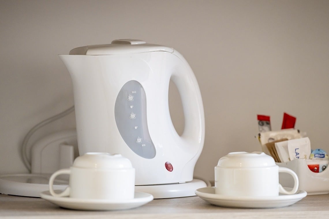 une bouilloire électrique blanche se trouve à côté de deux tasses de café
