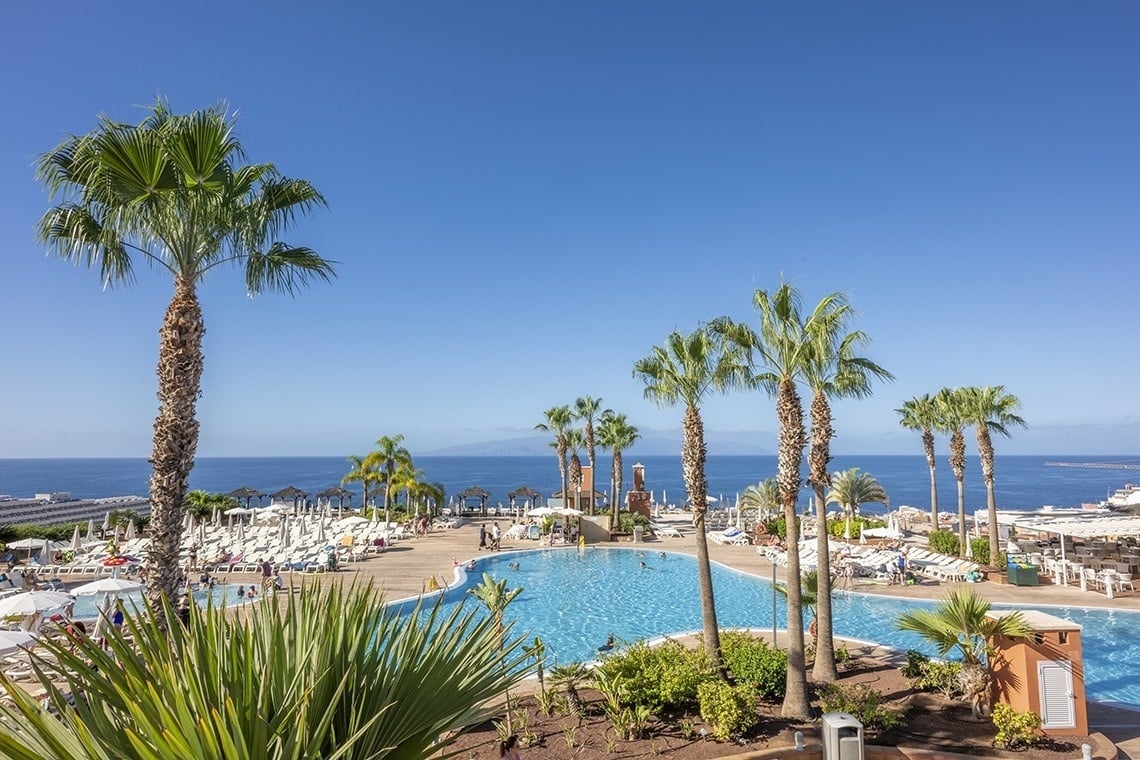 une grande piscine entourée d' arbres et de palmiers avec l' océan en arrière-plan