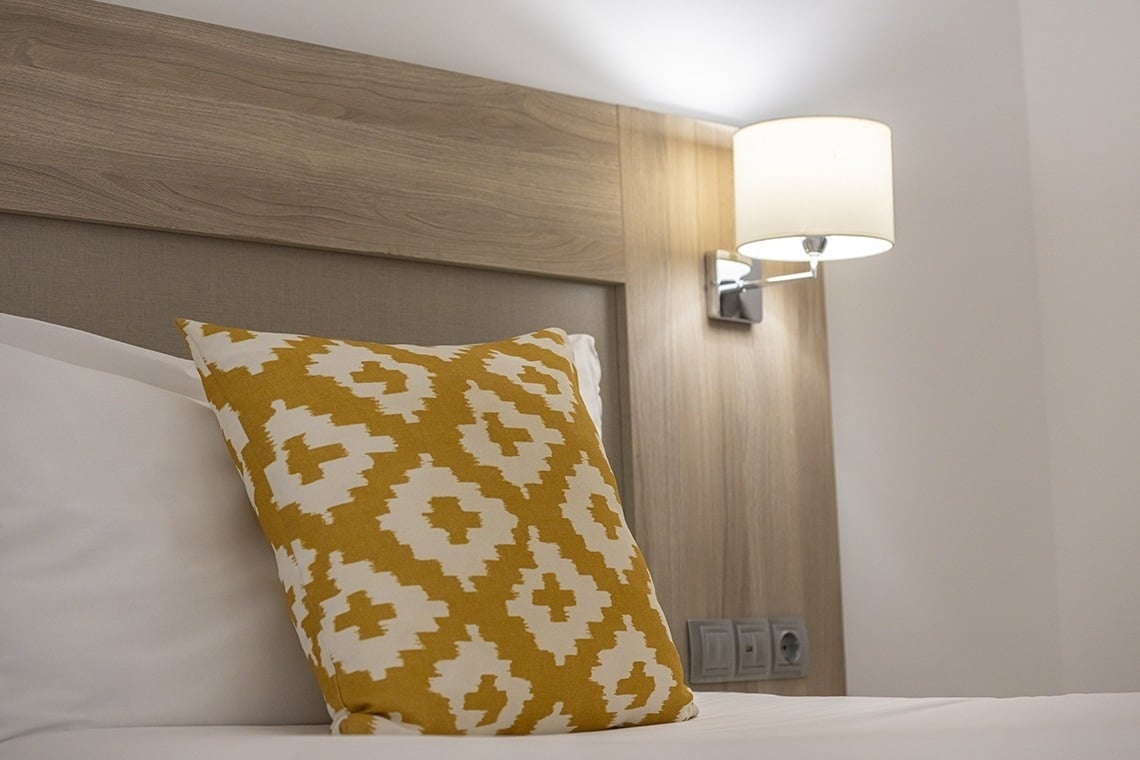 un oreiller jaune et blanc est posé sur un lit à côté d' une lampe