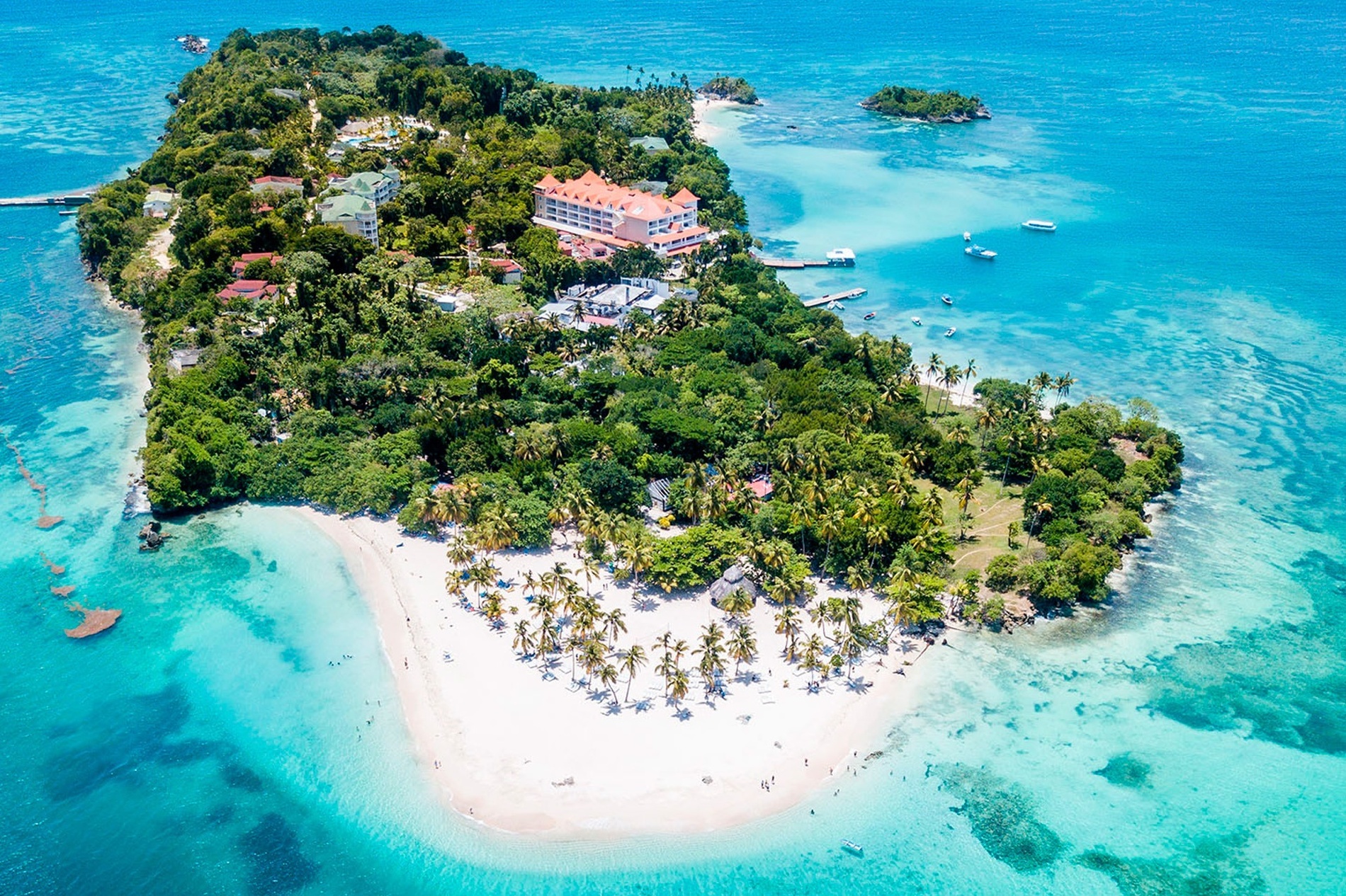 Aerial view of an island with a hotel in the middle surrounded by palm trees