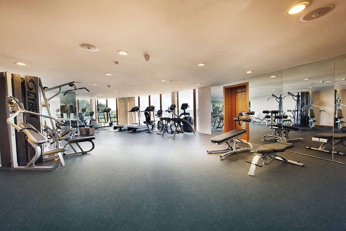This image captures a spacious and well-lit modern gym equipped with various exercise machines, large windows, and a mirrored wall.