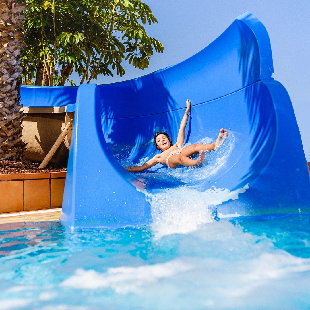 a young girl is sliding down a blue water slide