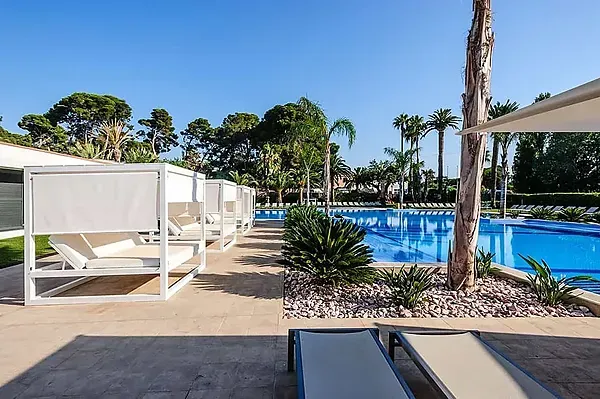 Estival: Corporatif, cabanes blanches près d'une piscine bleue vive avec chaises longues et palmiers.