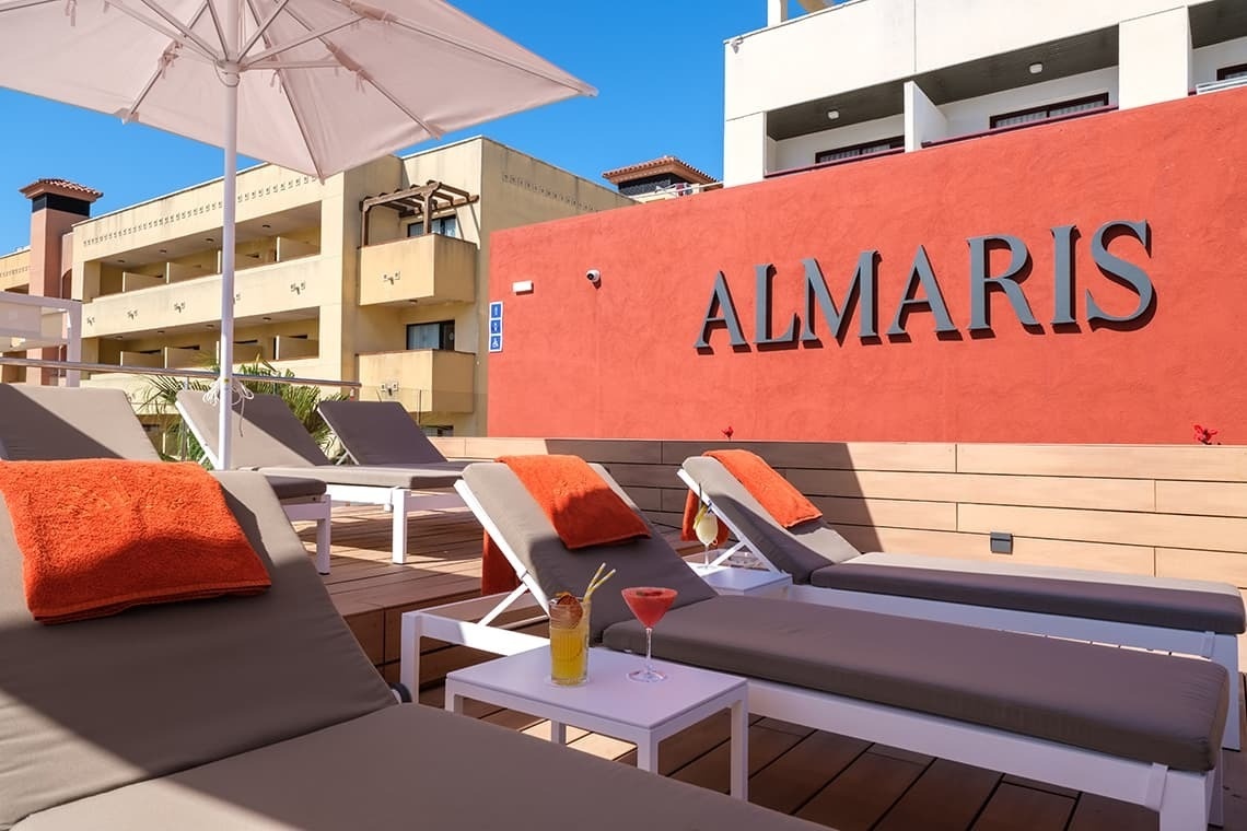 algunas tumbonas y una mesa con un cóctel frente a una pared roja que dice almaris