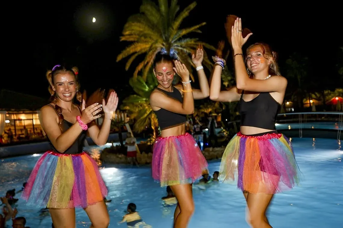 ESTIVAL: Corporativa. Drei junge Frauen in bunten Tutus feiern am Pool.