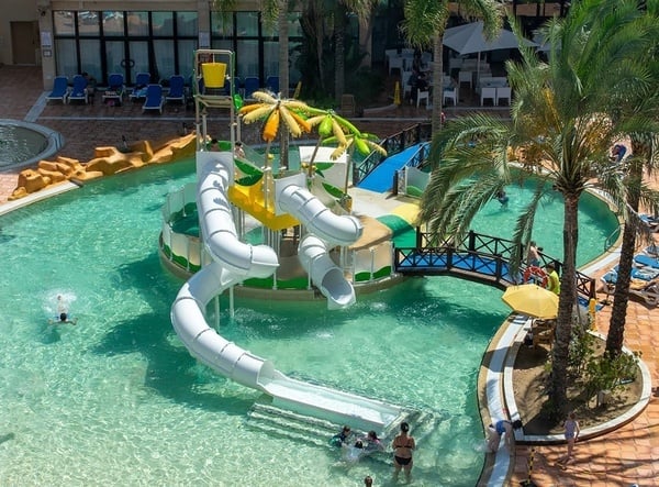 Kinder spielen in einem Wasserpark mit Rutsche und Palmen