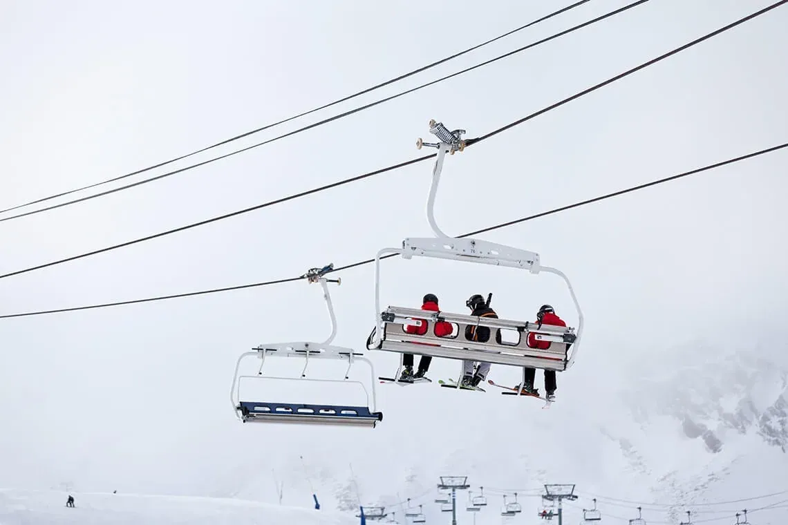 ESTIVAL: Firmenveranstaltung: Skifahrer im Sessellift mit Blick auf verschneite Berge.