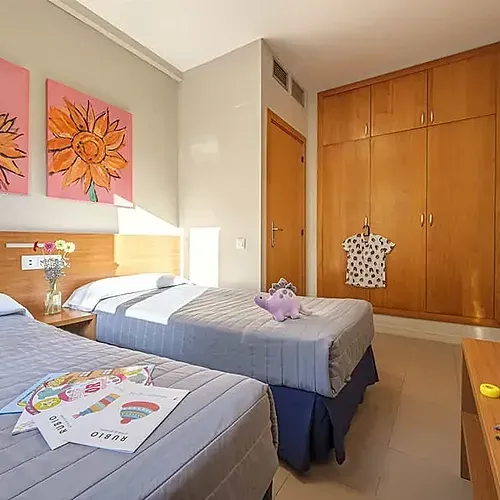 Habitació familiar ESTIVAL: dos llits, art de gira-sol, armari de fusta i joguines.
