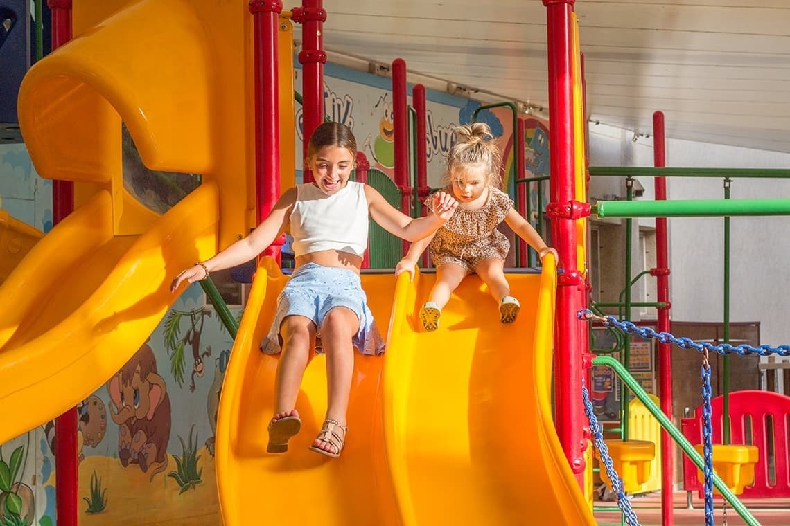 dos niñas juegan en un tobogán amarillo en un patio de recreo