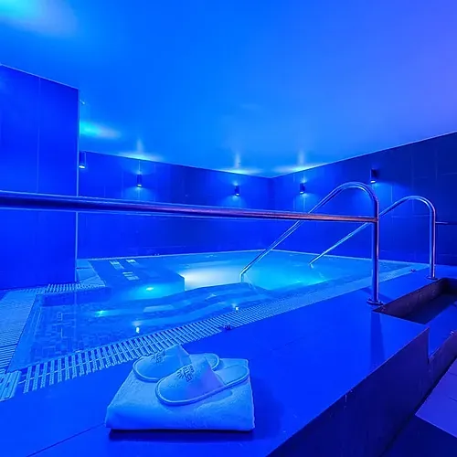 Indoor pool at Hotel Sporting Andorra with blue lighting, bathrobe & slippers.