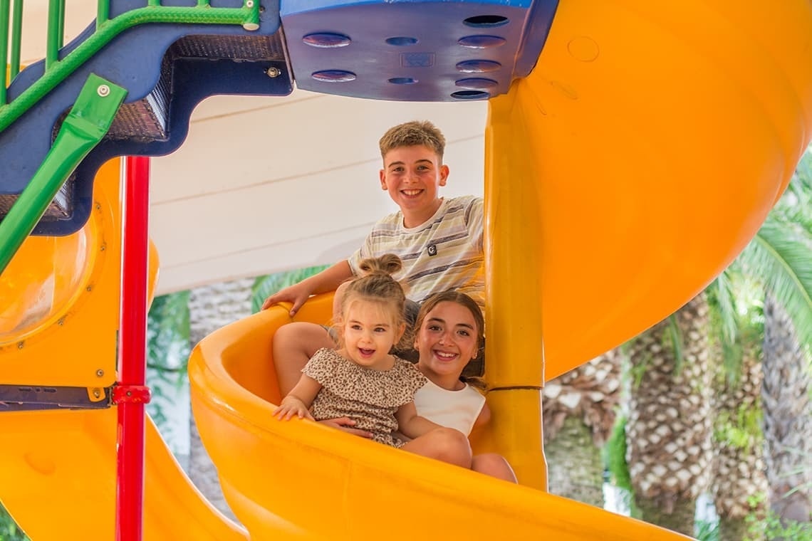 un niño y dos niñas se deslizan por un tobogán amarillo