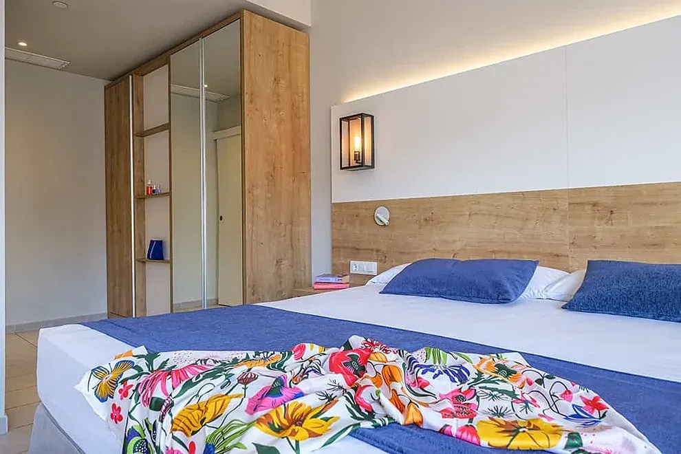 Habitación ESTIVAL: Corporativa, cama doble con edredón floral y armario espejo.
