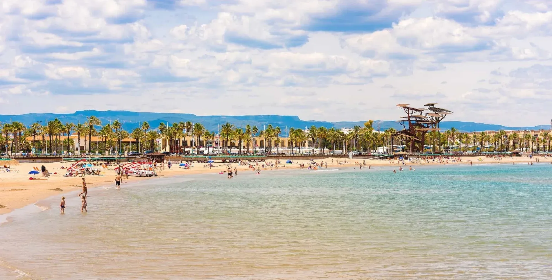 Plage animée avec palmiers et montagnes, près de notre Hôtel Oassium Platja de la Pineda.