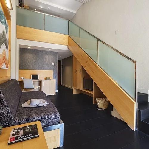 ESTIVAL: Corporate, modern hotel lounge with sofa, desk, and wooden stairs.