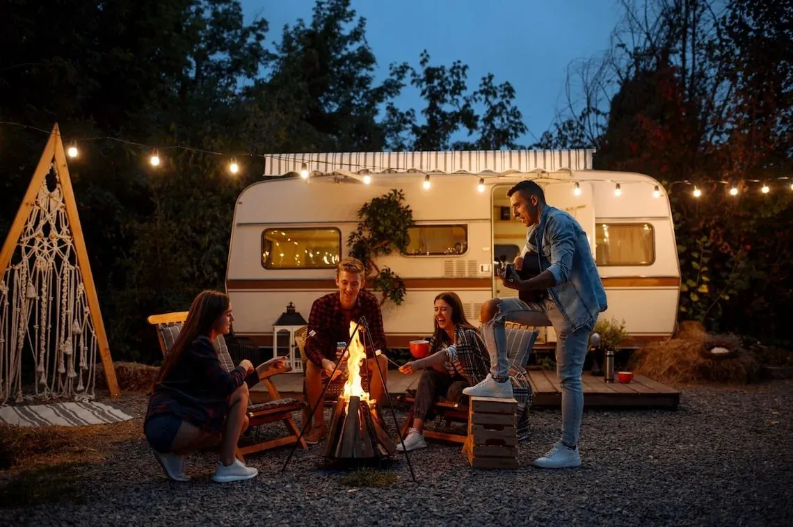 Amigos disfrutan fogata y música junto a caravana, perfecto para eventos ESTIVAL: Corporativa.