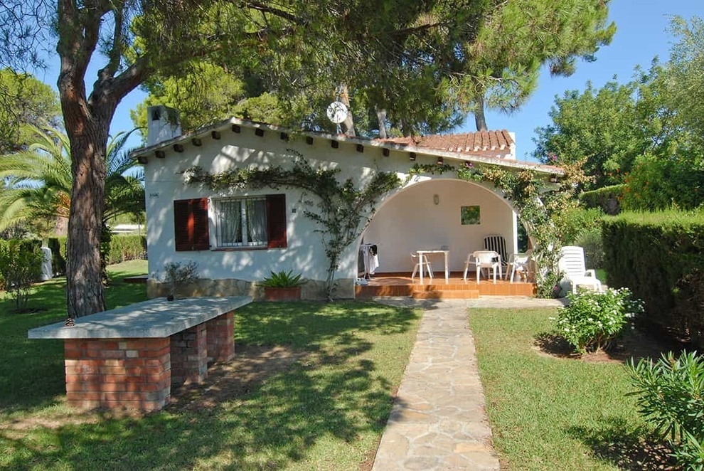 a small white house with red shutters sits in the middle of a lush green yard