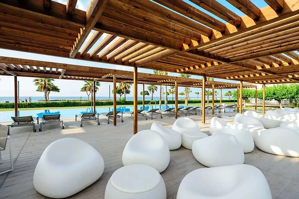 Chaises longues blanches modernes sous pergola bois, avec piscine et mer, parfait ESTIVAL: Corporativa.