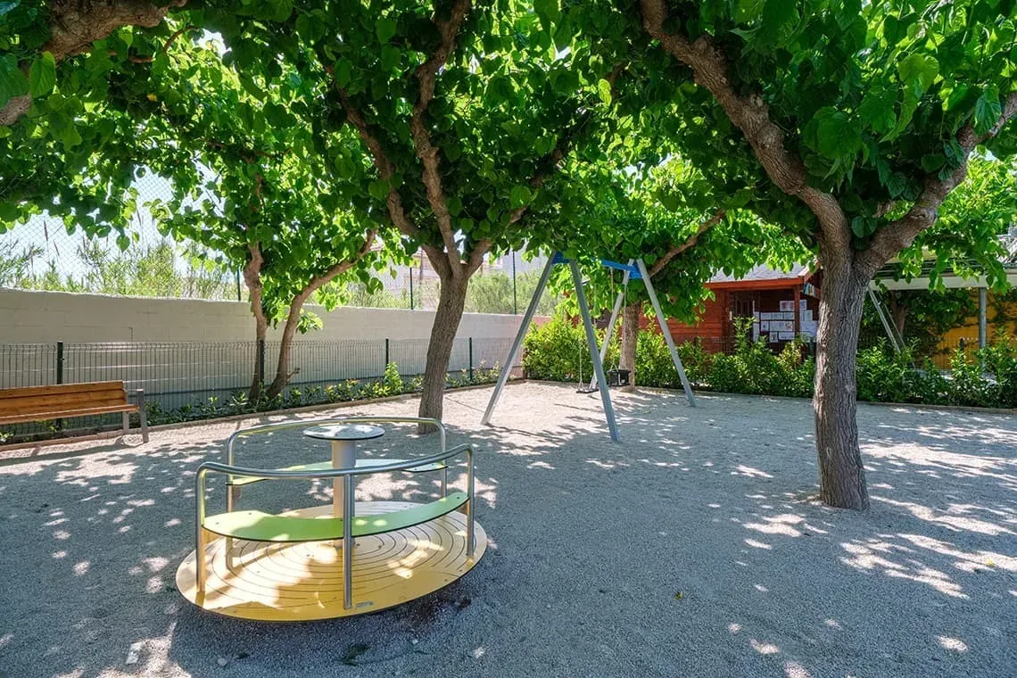 Parque infantil con tiovivo y columpios bajo árboles, ideal para ESTIVAL: corporativa.