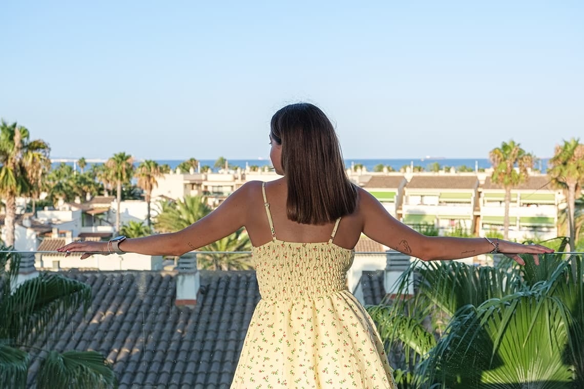 una mujer con un vestido amarillo se para en un balcón con los brazos extendidos