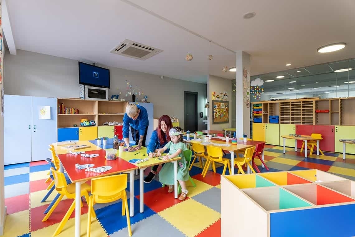 a woman and child are sitting at a table in a classroom