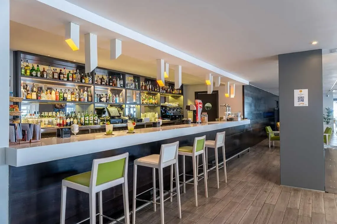 ESTIVAL: Corporativa moderne Bar mit Flaschen und grünen Hockern.