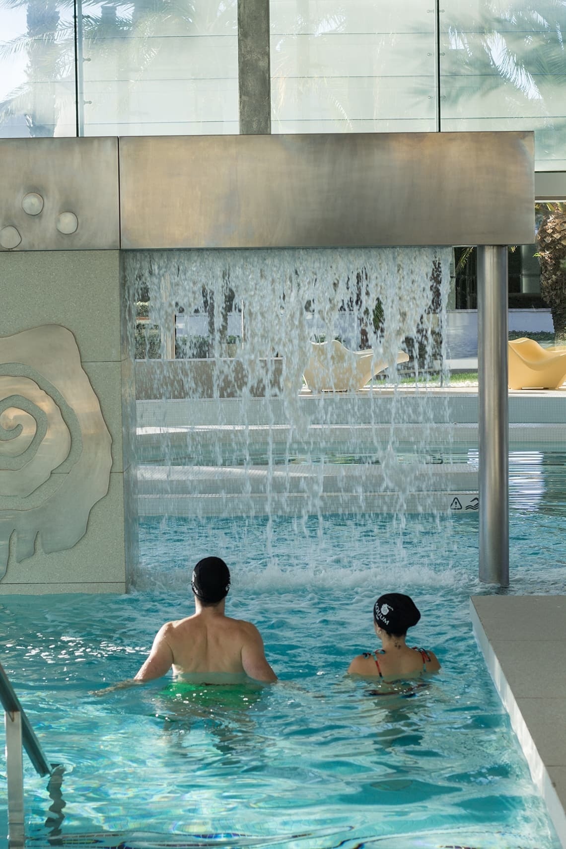 un hombre y una mujer nadan en una piscina junto a una cascada